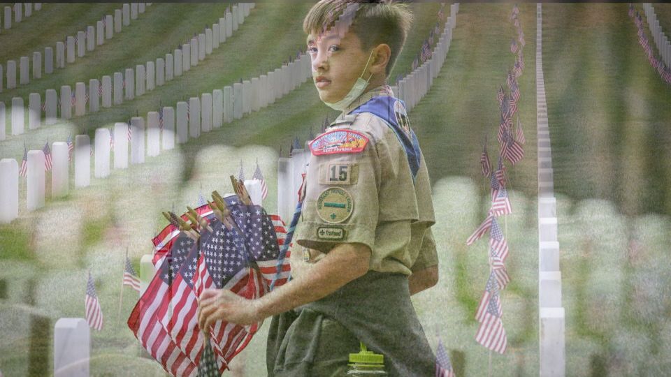 Scout holding USA flags to place at graves of fallen warriors on Memorial Day.